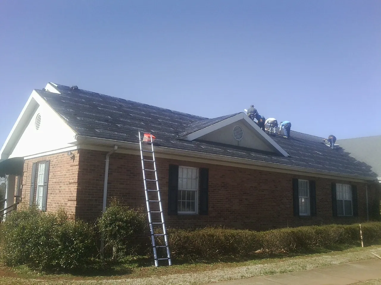 Crew tearing shingles off a brick ranch roof with a ladder set — Metal Roof Repair work by our crew in Ijamsville