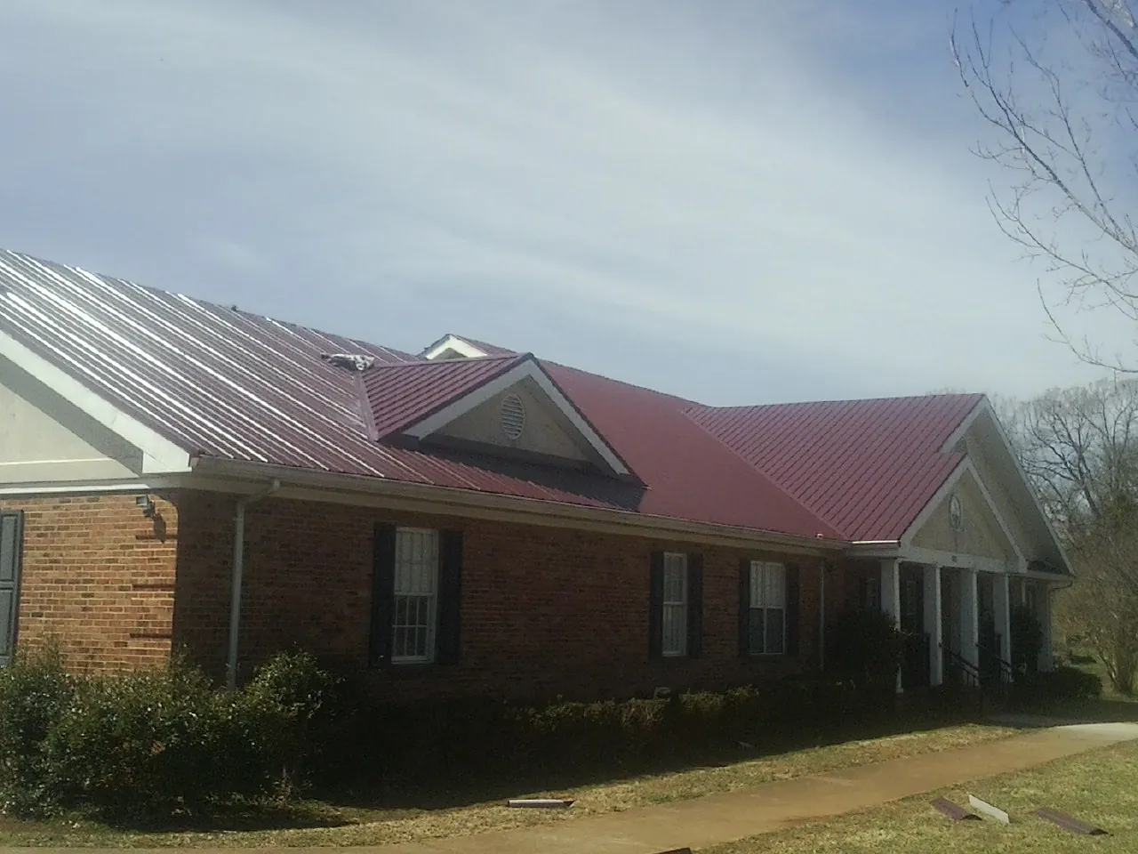 Red metal roof with gabled entries on a long brick building, from a Hail Damage Roof Repair job in Ijamsville