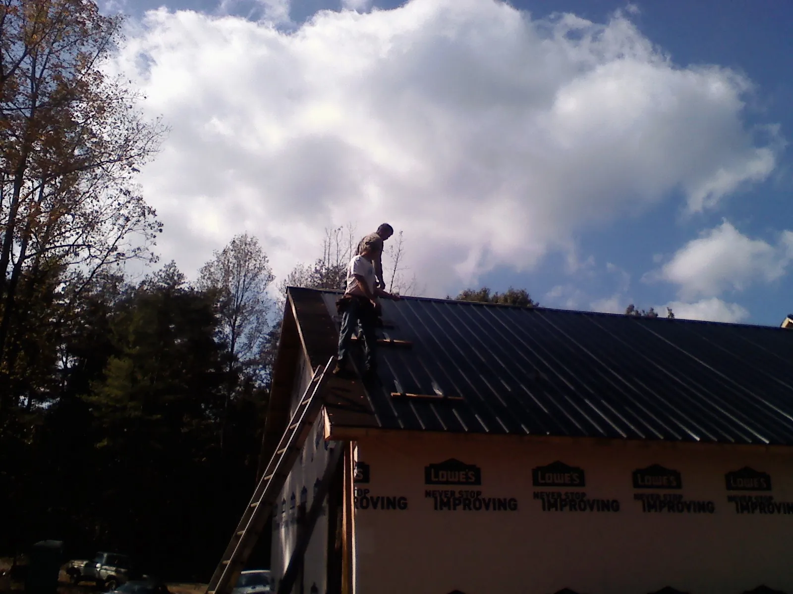 Roofer fastening dark metal panels high against a cloudy sky, from a Roof Inspection job in Ijamsville