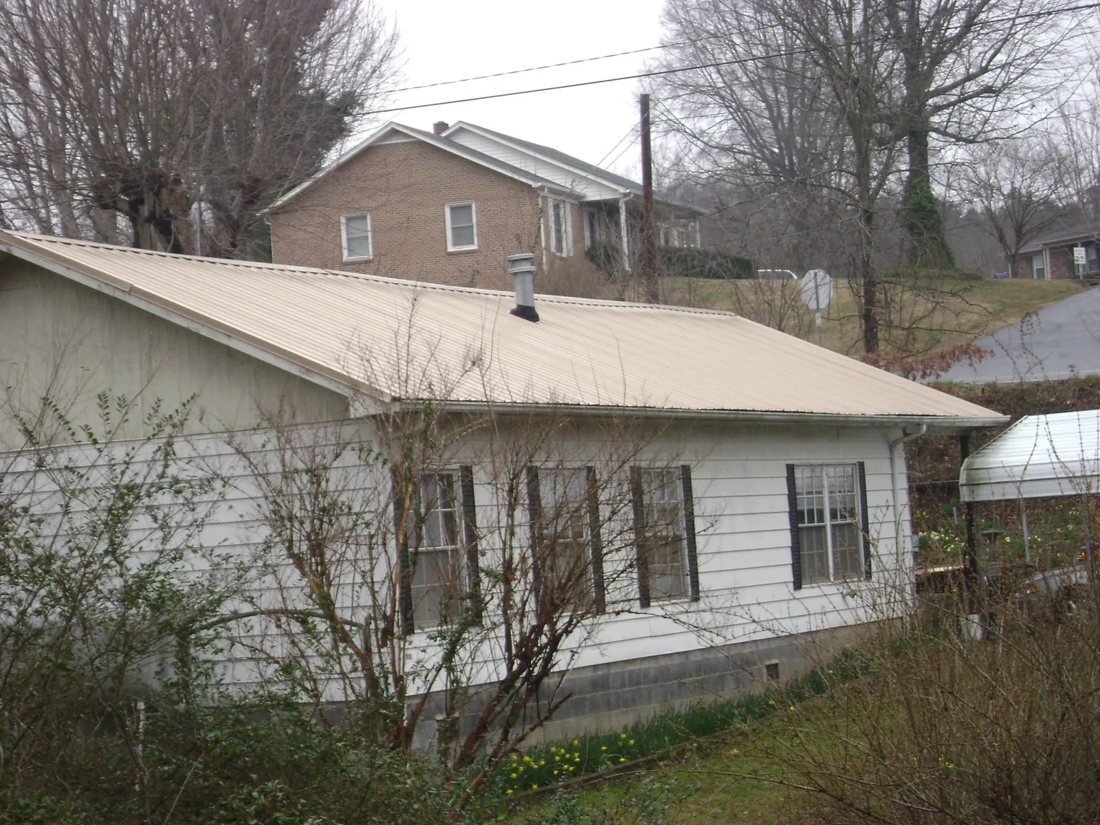 Tan metal roof on a white sided house set into a hillside — Commercial Roofing by Roofing Brothers in Ijamsville